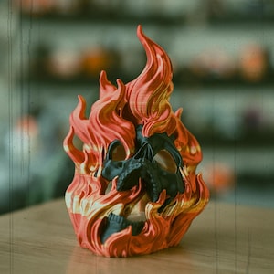 Könnte beinhalten: Eine 3D-gedruckte Schädelskulptur, die von Flammen umhüllt ist. Der Schädel ist schwarz und die Flammen sind rot und orange.