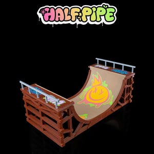 May include: A brown miniature half-pipe skate ramp with a smiley face graphic and the text "HALF PIPE" in a graffiti style. The ramp has a curved surface and a wooden frame with metal rails.