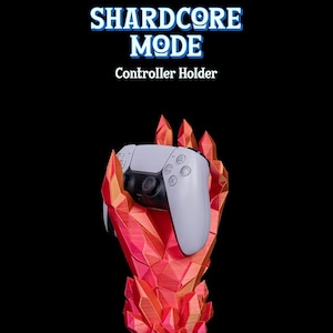 Peut inclure: Une main en cristal rouge tenant une manette de PlayStation 5 blanche. La main est faite d'un matériau imprimé en 3D et a une surface texturée. Le texte "SHARDCORE MODE" et "Controller Holder" est affiché au-dessus de la main.