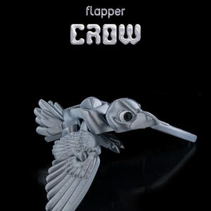 Puede incluir: Un juguete articulado en forma de cuervo de color plateado, con las alas extendidas. El juguete está hecho de plástico y tiene un diseño realista. El juguete está etiquetado como "flapper CROW" en letras plateadas.