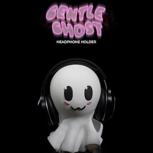 Op de afbeelding: Een witte, spookvormige koptelefoonhouder met zwarte koptelefoons en een schattig cartoon gezicht. De tekst "GENTLE GHOST HEADPHONE HOLDER" staat boven de geest.