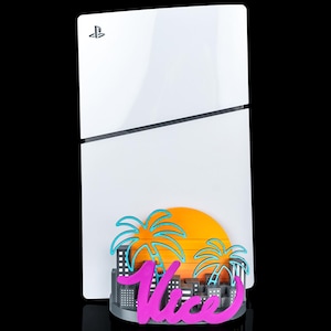 Op de afbeelding: Een witte PlayStation 5 console met een decoratieve bevestiging aan de basis. De bevestiging toont een gestileerde oranje zon, blauwe palmbomen, een grijze stadssilhouet en het woord Vice in felroze cursief schrift.