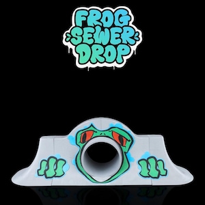 Può includere: Una rampa in cemento grigio con una grafica di un viso di rana verde e occhi rossi. La rampa ha un tunnel al centro. Il testo "Frog Sewer Drop" è scritto in blu e verde su sfondo bianco.