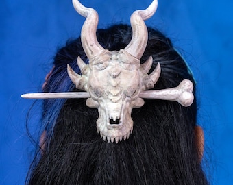 May include: A white dragon skull hair clip with a bone-like design. The clip is attached to a wooden stick.