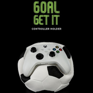 Könnte beinhalten: Weißer Xbox-Controller, der auf einem weißen und schwarzen Fußball liegt. Der Text "GOAL GET IT" und "CONTROLLER HOLDER" befindet sich über dem Ball.