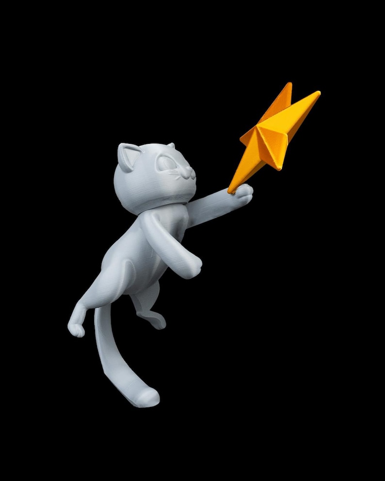 May include: A light gray cat figurine reaching for a bright yellow star. The cat is in a playful pose, with its tail curved and its front paws extended. The star has multiple points and a textured surface, set against a black background.