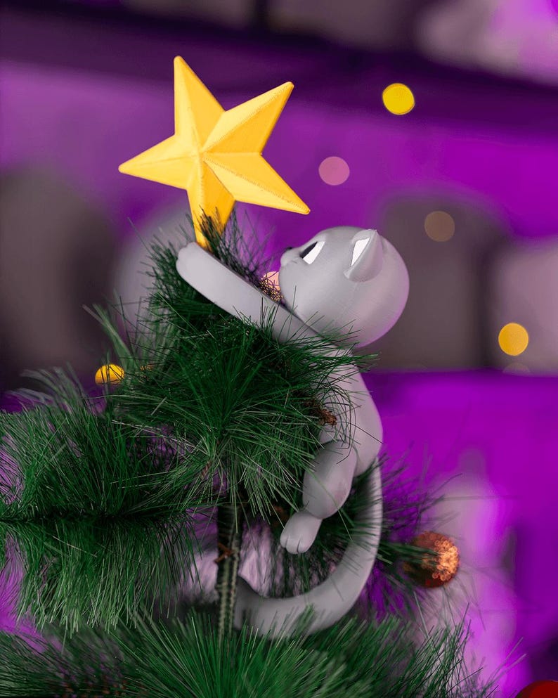 May include: A gray cat Christmas tree topper reaching for a yellow star. The cat is climbing a green artificial Christmas tree. The background is a blurred purple with yellow and orange bokeh lights.