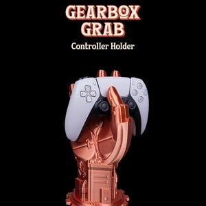 May include: A copper-colored controller holder in the shape of a mechanical hand, holding a white and black game controller. The base has a gear design. The text "GEARBOX GRAB Controller Holder" is at the top.