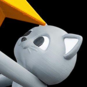 May include: A gray cat figurine with white ear and eye details, reaching for a yellow star. The cat has a friendly expression, set against a black background. The star is a bright yellow color.