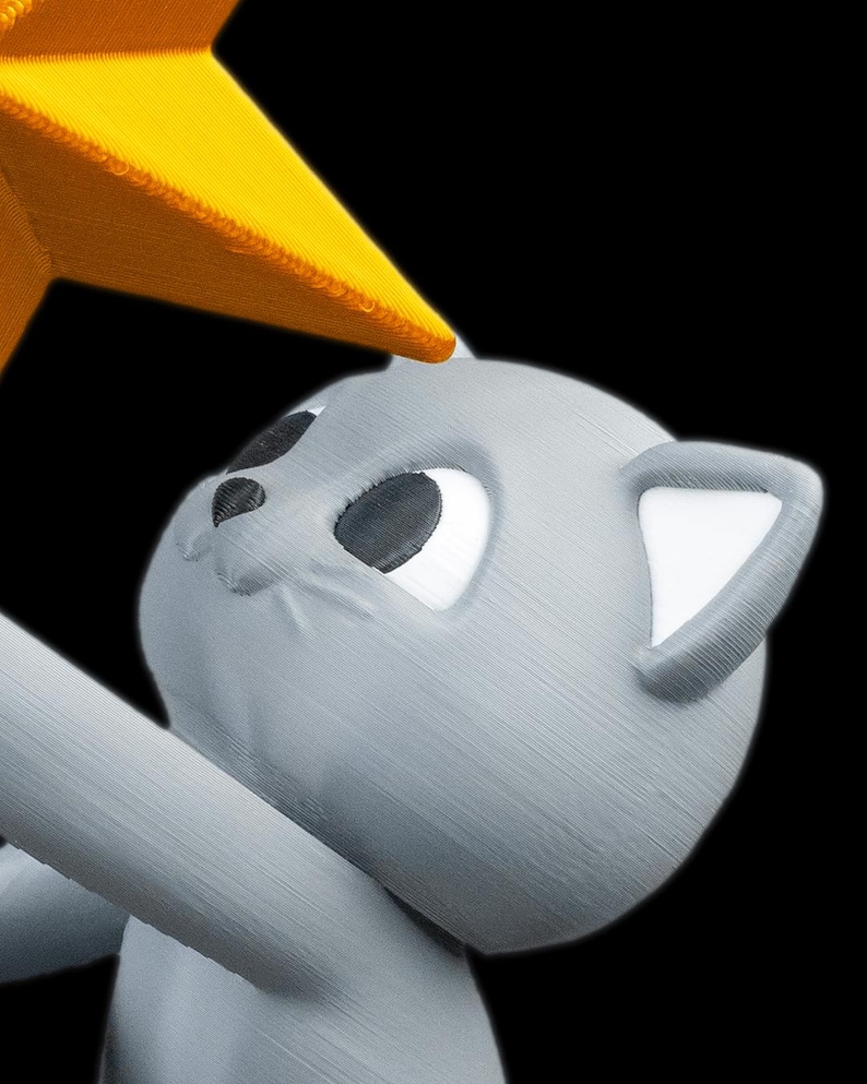 May include: A gray cat figurine with white ear and eye details, reaching for a yellow star. The cat has a friendly expression, set against a black background. The star is a bright yellow color.