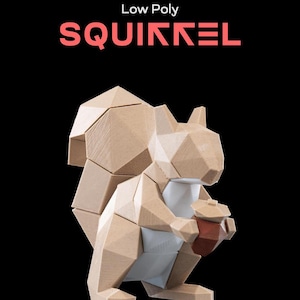 Może przedstawiać: Niskopoligonalny model wiewiórki trzymającej żołędź, Low Poly SQUIKKEL, wydrukowany w 3D. Wiewiórka jest wykonana z jasnobrązowego i białego plastiku i ma geometryczny wzór.