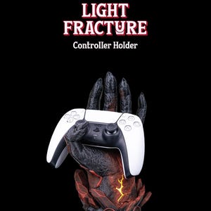 May include: A black and red hand-shaped controller holder with a white PlayStation 5 controller. The holder is designed to look like a hand emerging from a fiery, rocky base. The text "LIGHT FRACTURE" and "Controller Holder" is displayed above the holder.
