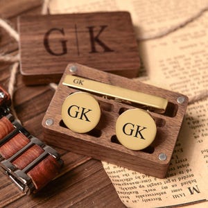 Può includere: Una scatola di legno con una spilla per cravatta e gemelli in oro. I gemelli e la spilla per cravatta sono incisi con le iniziali "GK".