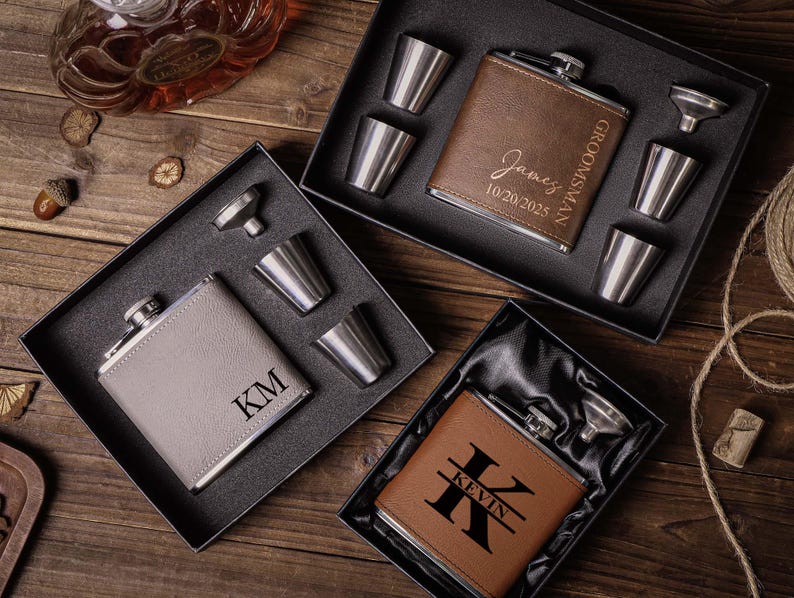 May include: Three gift sets for flasks with personalised engravings. Each set includes a flask, a funnel, and four shot glasses. The flasks are brown leather, grey leather, and brown leather with a black trim. The engravings on the flasks read "Groomman James 10.20.2025", "KM", and "Kevin".