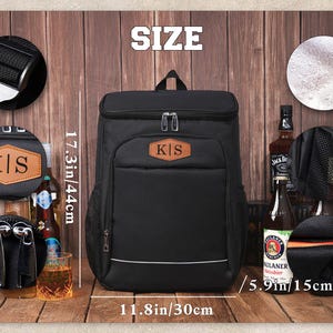 May include: Black insulated backpack with a brown leather patch displaying the initials "K|S". The backpack is 17.3 inches tall, 11.8 inches wide, and 5.9 inches deep. It has a top handle and a front pocket.
