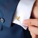 May include: Gold cufflinks with the letters "NC" intertwined. The cufflinks are worn on a white dress shirt.