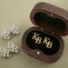 May include: A wooden box with a black velvet interior, containing two gold cufflinks engraved with the initials "KB".  The box is open, revealing the cufflinks.  Four silver cufflinks engraved with the initials "JZ" and "DR" are also shown.