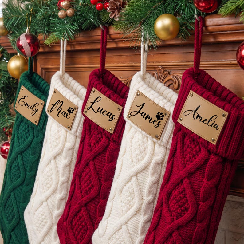 May include: Five cable-knit Christmas stockings in green, white, red, white, and red. Each stocking features a rectangular tan leather tag with the names Emily, Max with a paw print, Lucas, James with a paw print, and Amelia in black script.