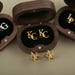 May include: Three wooden boxes with black velvet interiors, each containing a pair of gold cufflinks with different initials. The initials are "AG", "KC", and "LP".