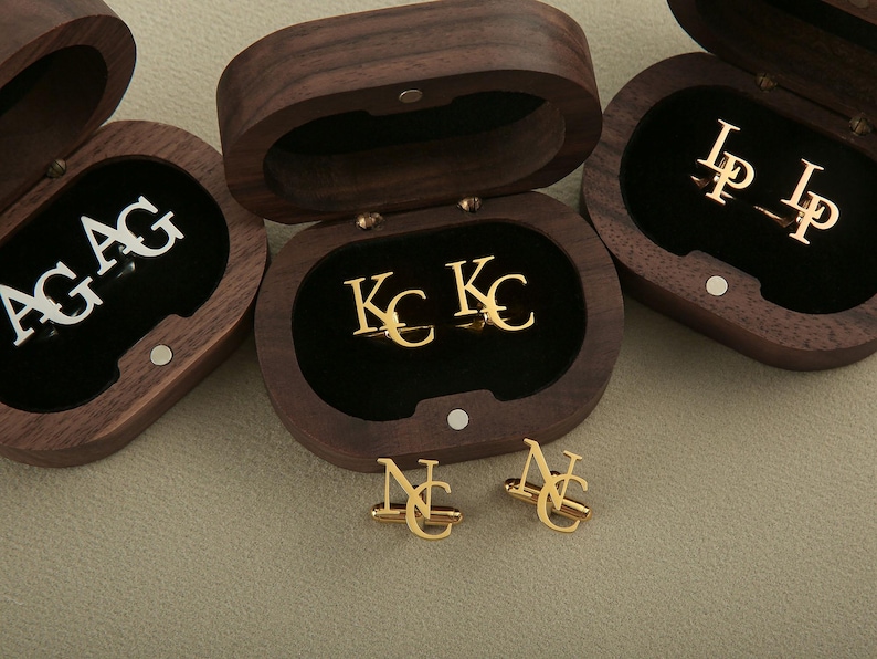 May include: Three wooden boxes with black velvet interiors, each containing a pair of gold cufflinks with different initials. The initials are "AG", "KC", and "LP".