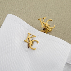 May include: A pair of gold cufflinks with the letters "KC" engraved on them.