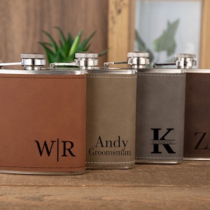 May include: Four personalized stainless steel hip flasks with brown, gray, and green leatherette coverings. The flasks are engraved with the initials "W|R", "Andy Groomman", "K KENNETH", and "ZR".