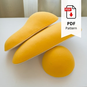 Può includere: Tre forme di tessuto giallo, tra cui due pezzi allungati e una forma arrotondata, sono disposte su una superficie bianca. L'immagine include un'icona del modello PDF con il testo "PDF Pattern".