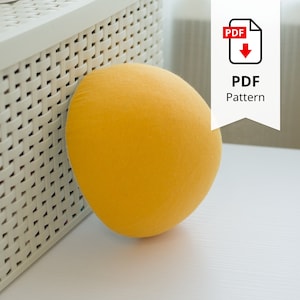 May include: A round, yellow cushion rests on a white surface next to a white woven basket. The cushion has a soft, textured appearance. A white banner with the text "PDF Pattern" and a PDF icon is in the upper right corner.