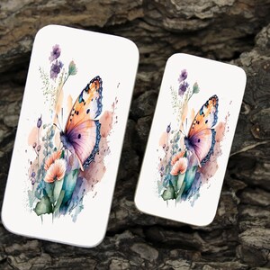 Puede incluir: Una ilustración de acuarela de una mariposa con alas naranja y rosadas, posada sobre una flor con hojas verdes y flores moradas. El fondo es una suave acuarela de azul y rosa.