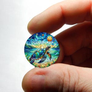 May include: A round, colorful stained glass design featuring a sea turtle swimming in the ocean. The turtle is blue, green, and yellow. The ocean is blue and green, with a yellow sun in the background. The design is surrounded by a white border.
