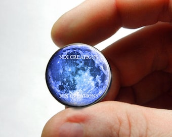 May include: A close-up of a blue glass cabochon with a moon image and the text "NIX CREATIONS" printed on it.