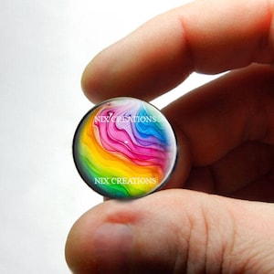 May include: A colorful glass cabochon with a rainbow abstract design. The cabochon is round and has a glossy finish. The design features swirls of pink, blue, yellow, green, and orange.