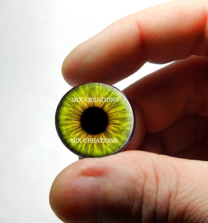 May include: A yellow and black eye-shaped glass cabochon with the text "NIX CREATIONS" printed on the top and bottom.