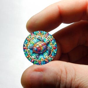 May include: A colourful stained glass style turtle design on a round, blue, green, yellow, and pink background.