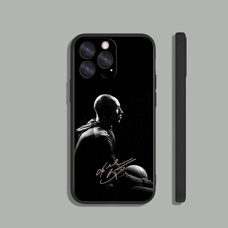 May include: Black and white phone case with a silhouette of a basketball player holding a basketball. The player's signature is in gold lettering.