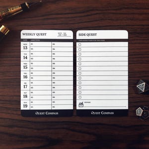 May include: Two white and black Quest Compass weekly and side quest cards with a wooden background. The weekly quest card has a calendar layout. Two dice and a pen are also on the wooden surface.