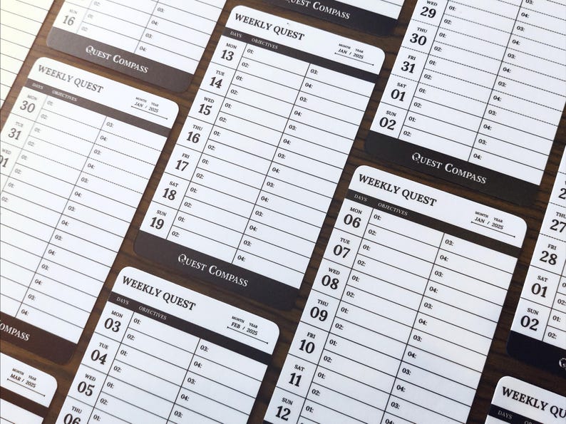 May include: Several white and black weekly planner cards with the text "Weekly Quest" and "Quest Compass". Each card has dates and space for objectives. The cards are arranged on a dark brown surface.