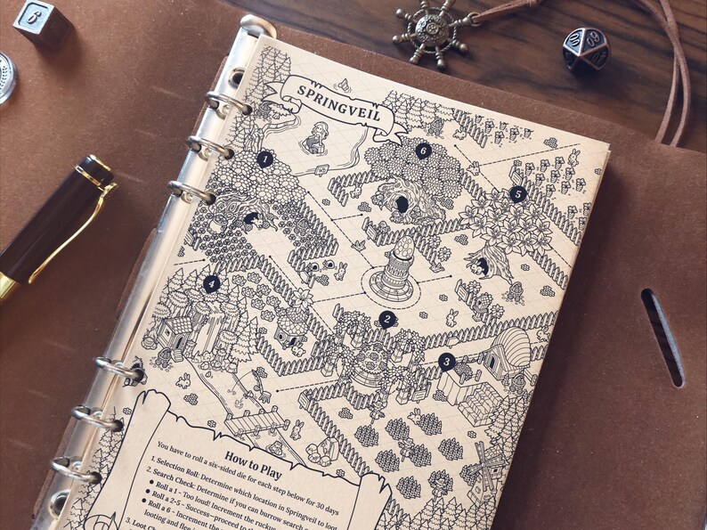 May include: A detailed black and white map of Springveil, a fantasy game, is displayed in a binder. The map features numbered locations, trees, buildings, and a banner with the game's name. A pen, dice, and a compass charm are also visible.