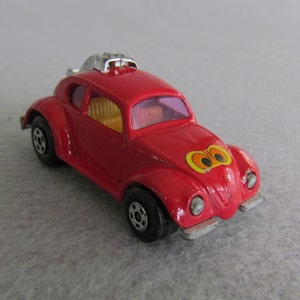 May include: Red toy car with a black roof and black wheels. The car has a sticker of two eyes on the front.
