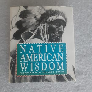 May include: A book titled "Native American Wisdom" with a black and white photograph of a Native American man wearing a headdress. The book cover has a turquoise and white text box with the title and the author's name, Edward S. Curtis.