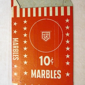 May include: A red and white cardboard box with a white circle in the center. The circle contains the text "Made in U.S.A." in a shield shape. The box has the text "10¢ MARBLES" in white letters. The box is decorated with white stars and stripes.