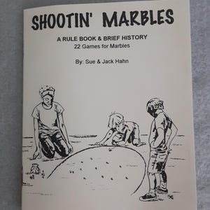 Puede incluir: Un libro vintage titulado "Shootin' Marbles" con una ilustración en blanco y negro de niños jugando a las canicas. La portada incluye el texto "A Rule Book & Brief History, 22 Games for Marbles" y los nombres de los autores.