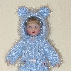 May include: A doll wearing a light blue knitted coat with a hood and bear ears. The coat has bear-shaped buttons and small floral accents. The doll is wearing white socks and tan shoes with pink laces. The outfit is approximately 10 inches in height.