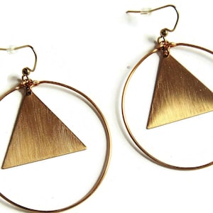 May include: Gold hoop earrings with a brushed gold triangle pendant hanging from each hoop.