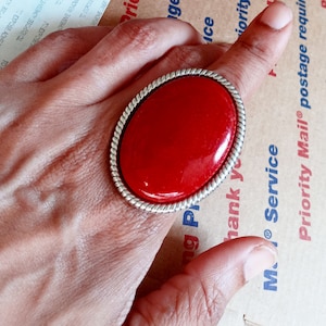 May include: A large, red oval ring with a silver band. The ring is set with a red stone and has a rope-like design around the edge.