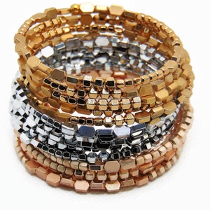 May include: A stack of gold, silver, and rose gold bracelets made of small, hexagonal beads.