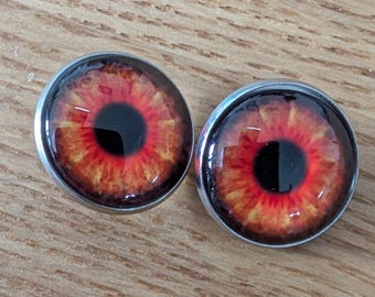 May include: Two round, silver-colored buttons with red and orange eye designs. The eyes have black pupils and a red iris.