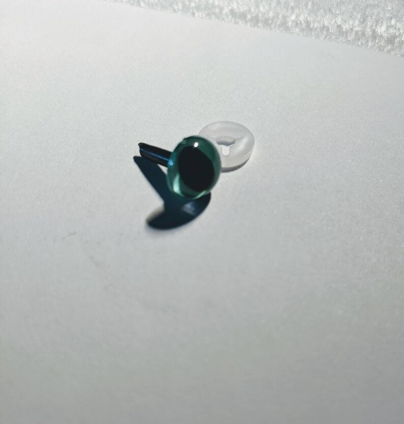 May include: A single green plastic safety eye with a black pupil and a white plastic washer.