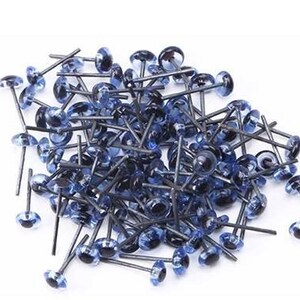 May include: A large pile of blue plastic safety eyes with black pupils and metal shanks. The eyes are used for craft projects such as stuffed animals and dolls.