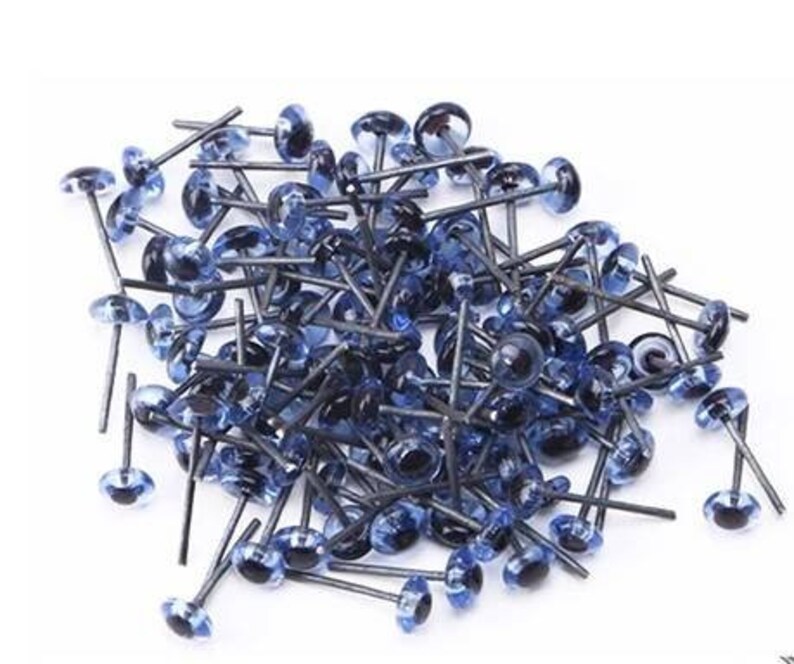 May include: A large pile of blue plastic safety eyes with black pupils and metal shanks. The eyes are used for craft projects such as stuffed animals and dolls.